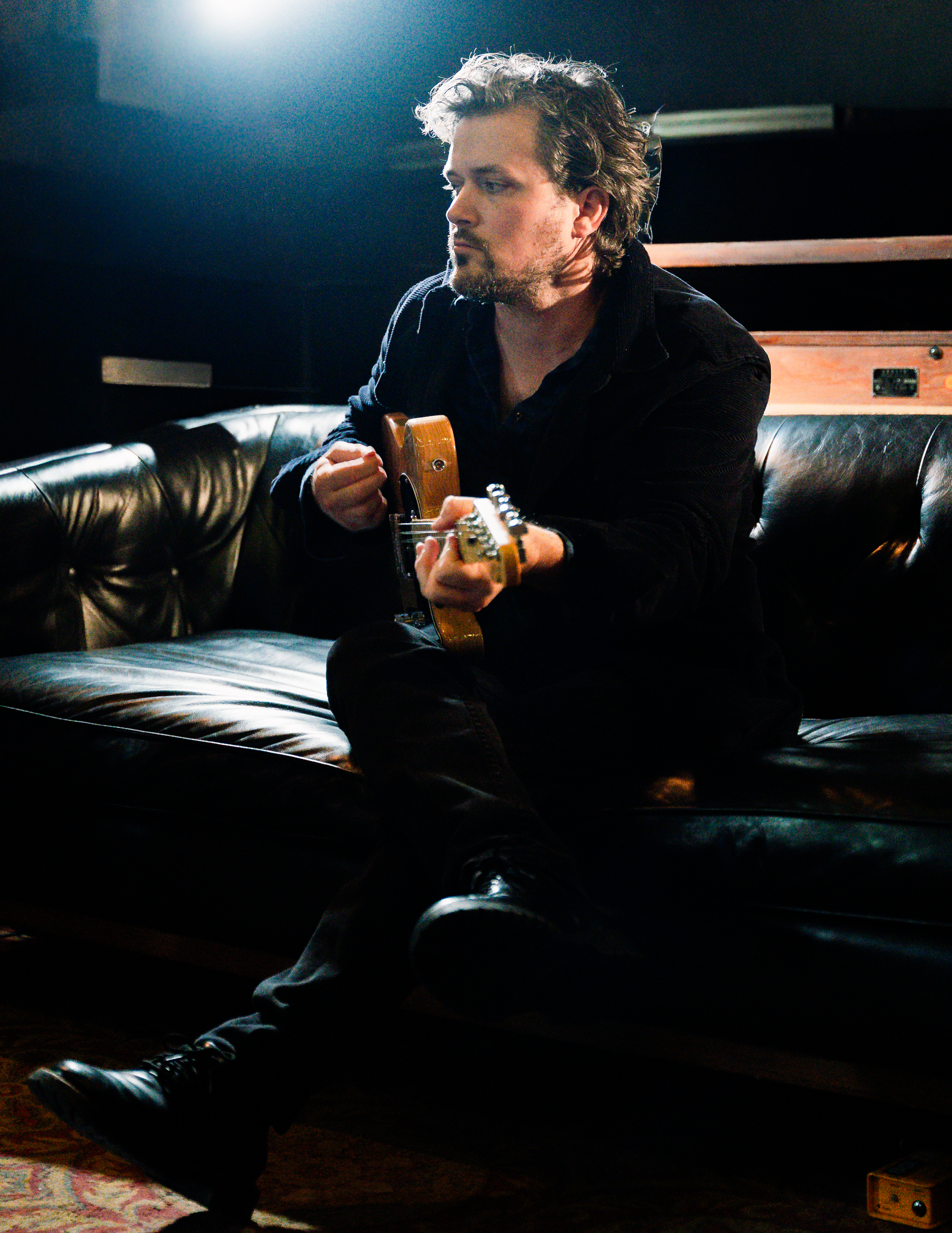 Kingston seated on a studio couch holding a guitar
