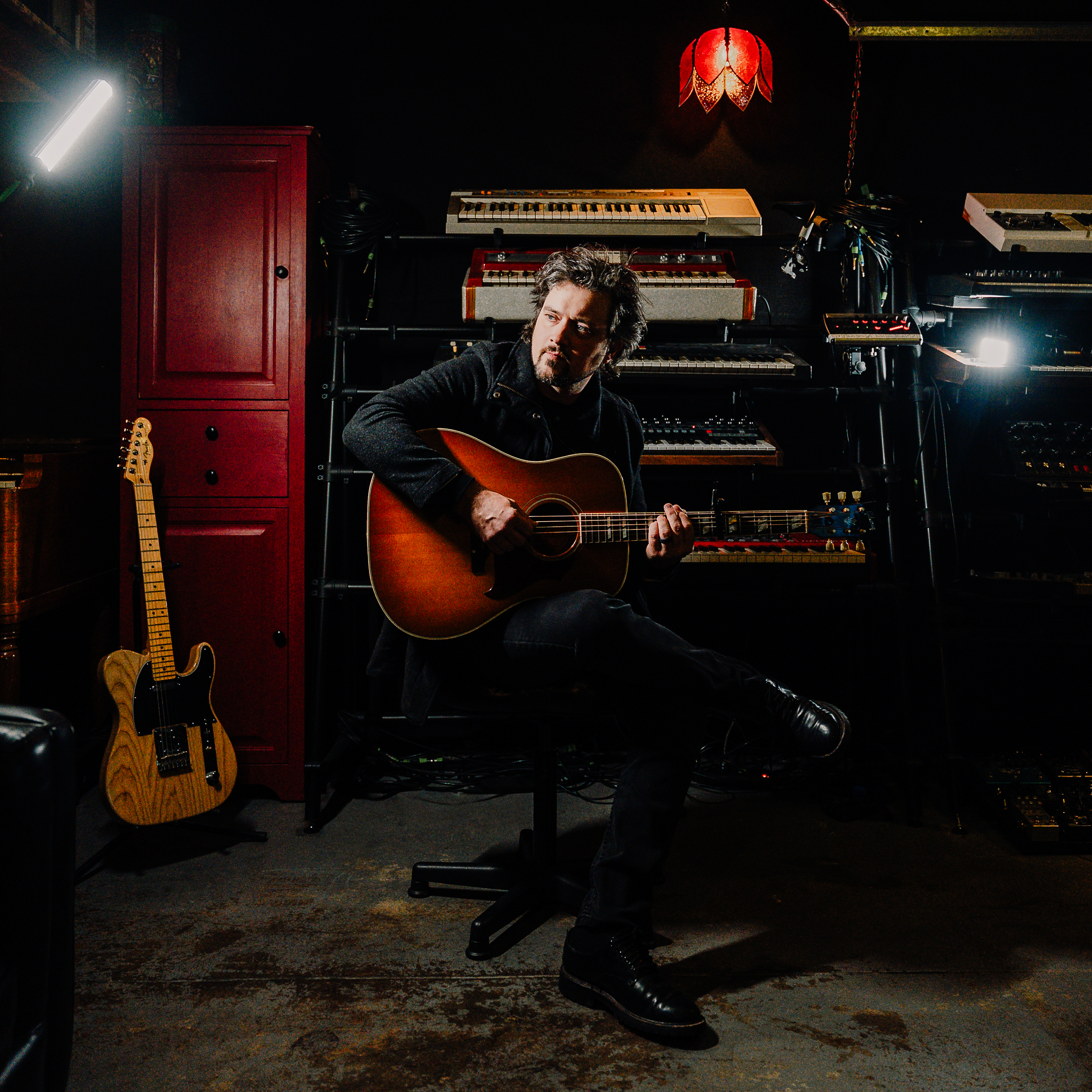 Kingston seated in a studio holding an acoustic guitar